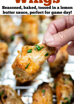 Pinterest pin with a hand holding a chicken wing above a baking rack of cooked chicken wings topped with fresh parsley.