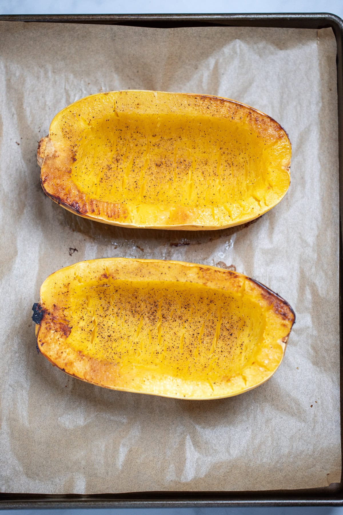 Roasted spaghetti squash on a sheet pan lined with parchment paper, fresh out of the oven before being scooped out.