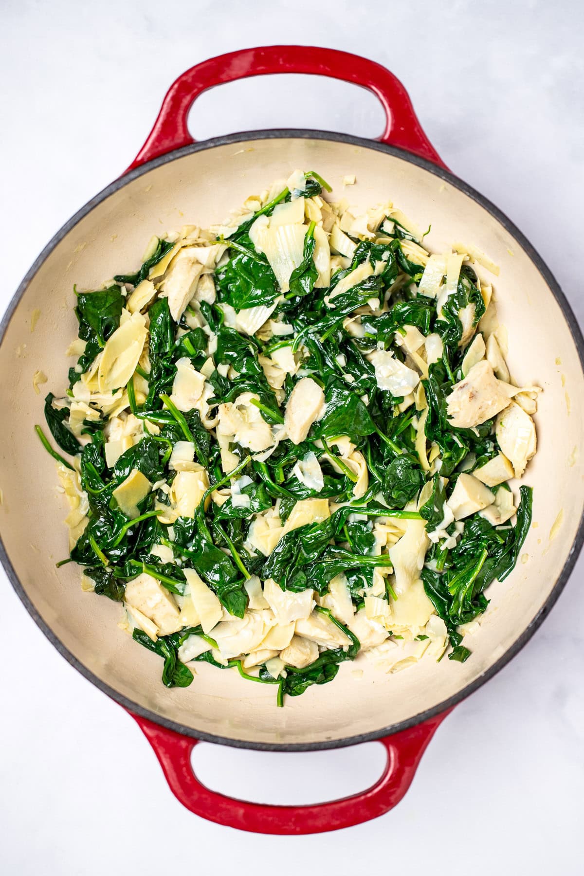 A dutch oven full of cooked spinach and chopped artichoke hearts.