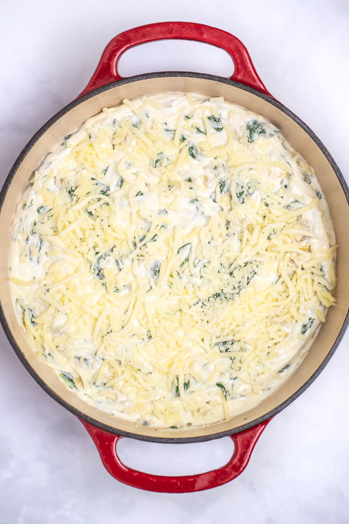 A dutch oven with spinach artichoke dip topped with shredded mozzarella cheese before baking.