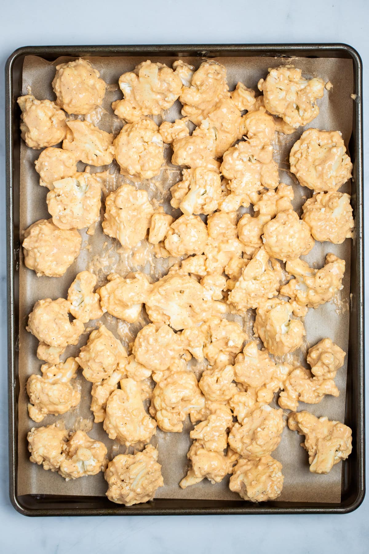 Battered cauliflower florets on a sheet pan lined with parchment paper, in a single layer, before being baked.