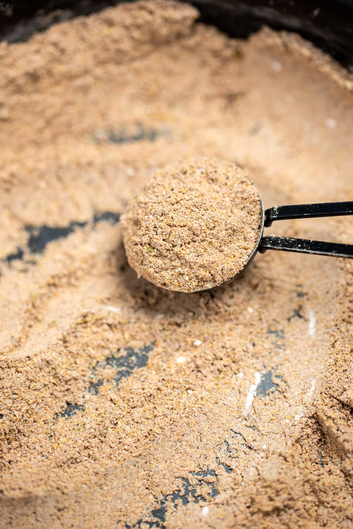 A closeup in a bowl of fajita seasoning, with a tablespoon full of seasoning resting in the bowl.