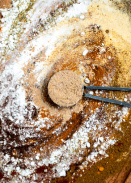 Fajita seasoning spices on a cutting board being mixed together, with a tablespoon of seasoning resting in the middle.