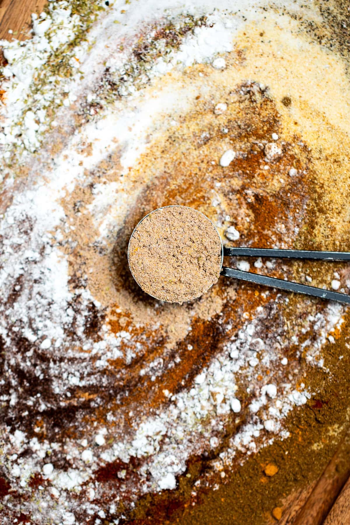 Fajita seasoning spices on a cutting board being mixed together, with a tablespoon of seasoning resting in the middle.