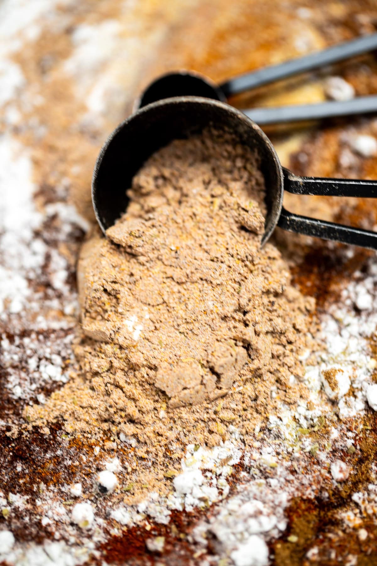 Fajita seasoning pouring out of a tablespoon that's resting on a cutting board.