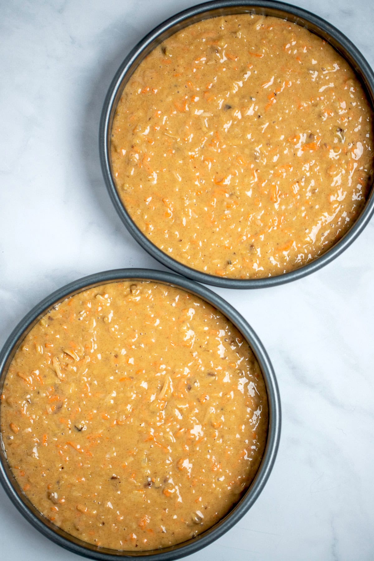 Two cake pans filled with carrot cake batter before being baked.