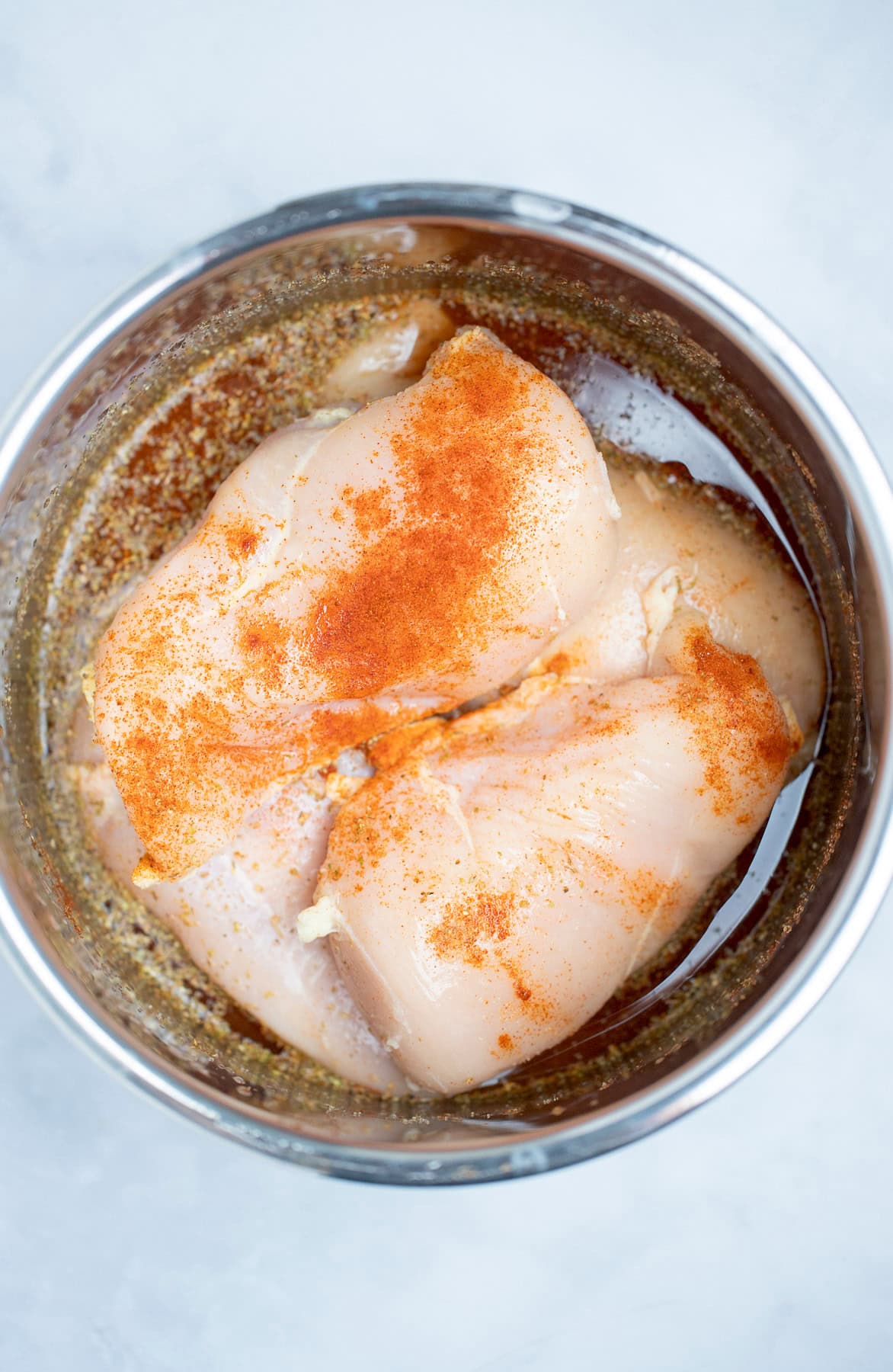 An instant pot pot with raw chicken breast, water, and spices before being cooked.