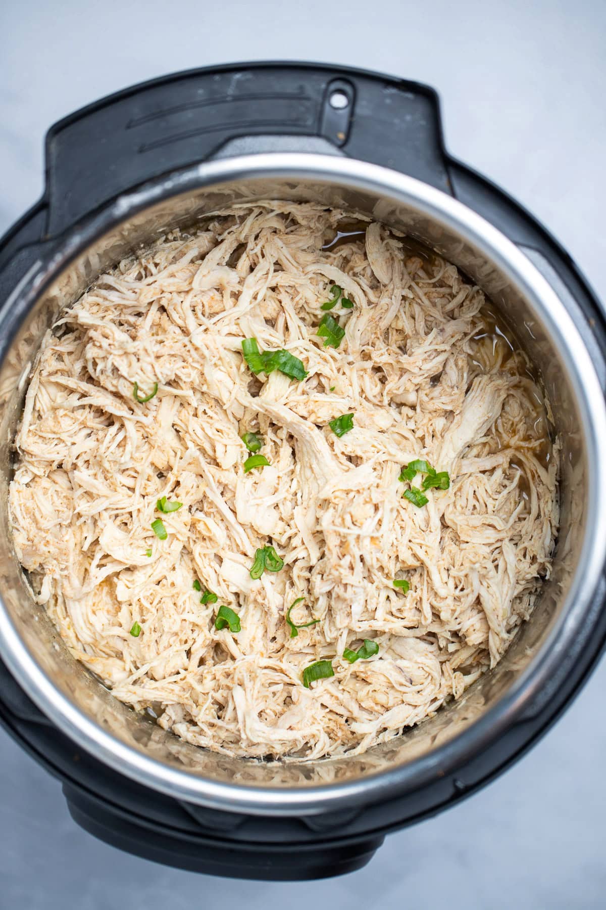 An instant pot with shredded chicken breast topped with fresh chopped green onions.