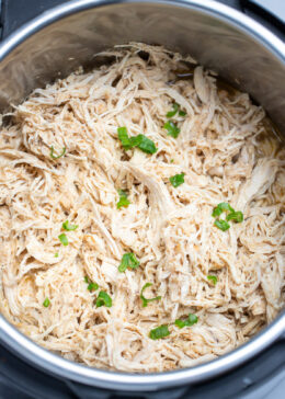 An instant pot with shredded chicken breast topped with fresh chopped green onions.