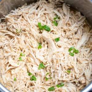 An instant pot with shredded chicken breast topped with fresh chopped green onions.