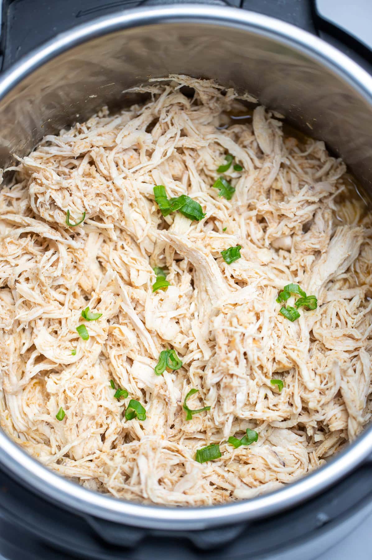 An instant pot with shredded chicken breast topped with fresh chopped green onions.