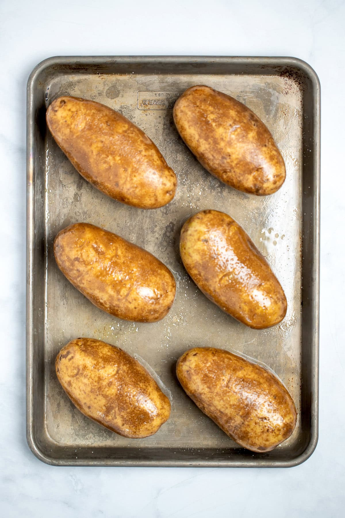 Russet potatoes coated in olive oil and salt on a sheet pan before being baked.