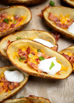 Loaded potato skins topped with cheese, bacon, green onions, and sour cream on a sheet pan.