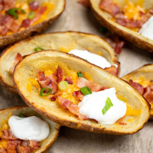 Loaded potato skins topped with cheese, bacon, green onions, and sour cream on a sheet pan.