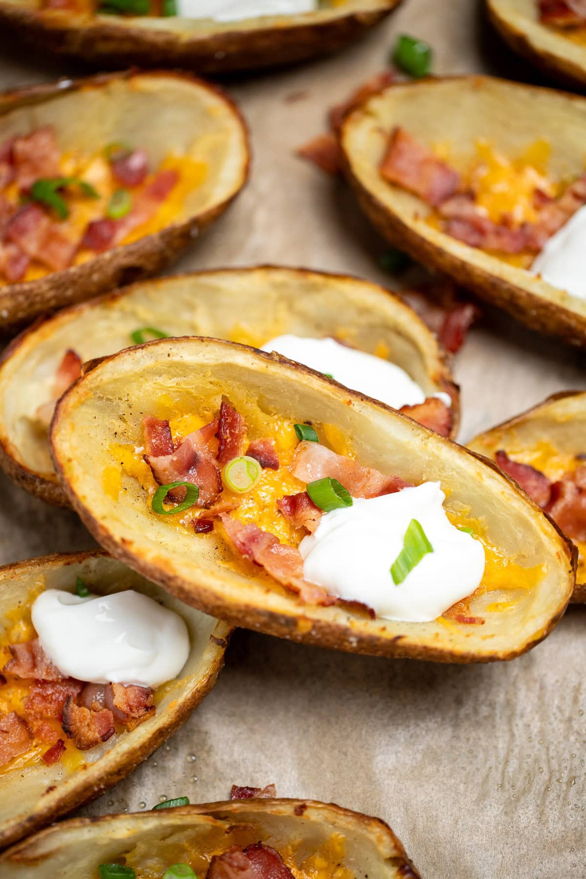 Loaded potato skins topped with cheese, bacon, green onions, and sour cream on a sheet pan.