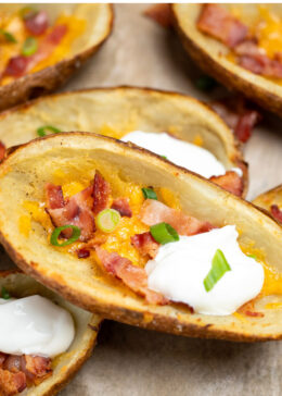 Pinterest pin with loaded potato skins topped with cheese, bacon, green onions, and sour cream on a sheet pan.