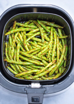 An air fryer basket with green beans air fried with olive oil and spices.