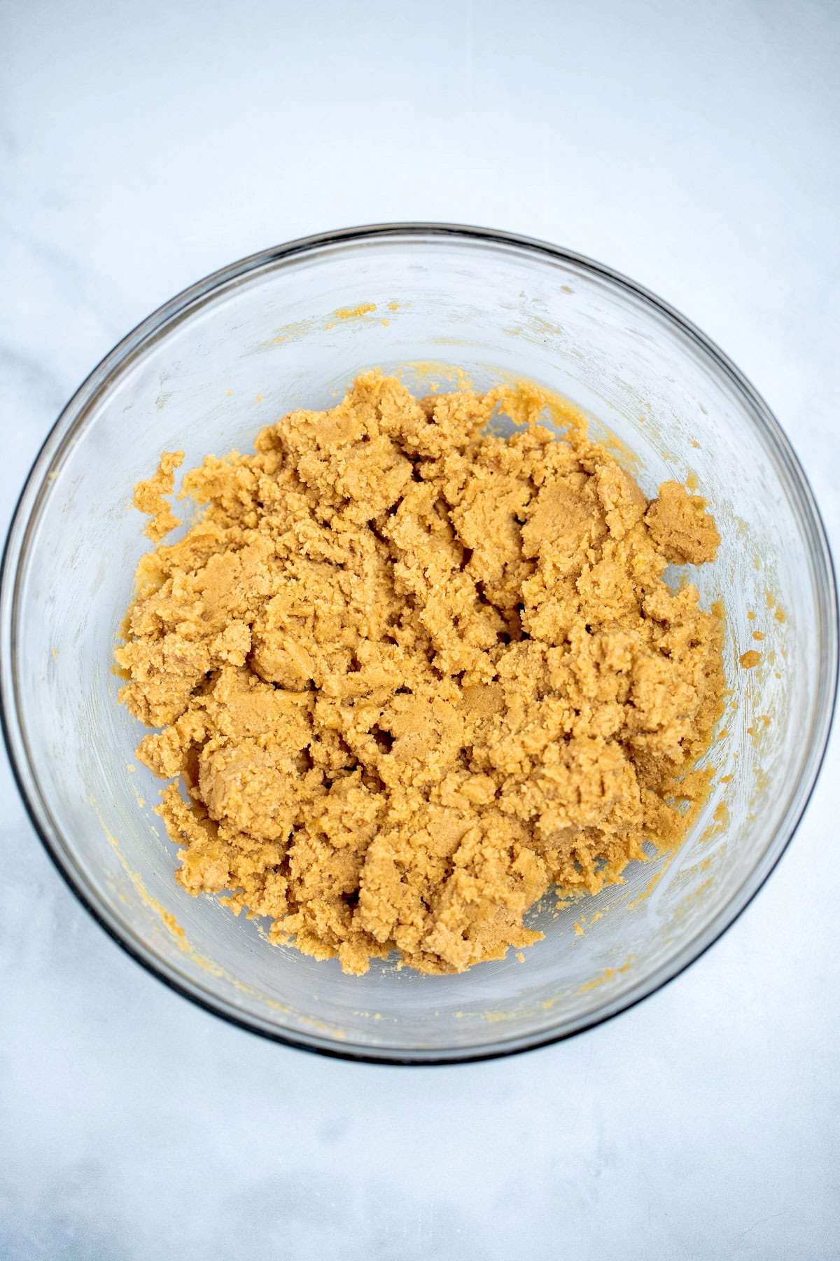 A glass mixing bowl with cookie dough on a table.