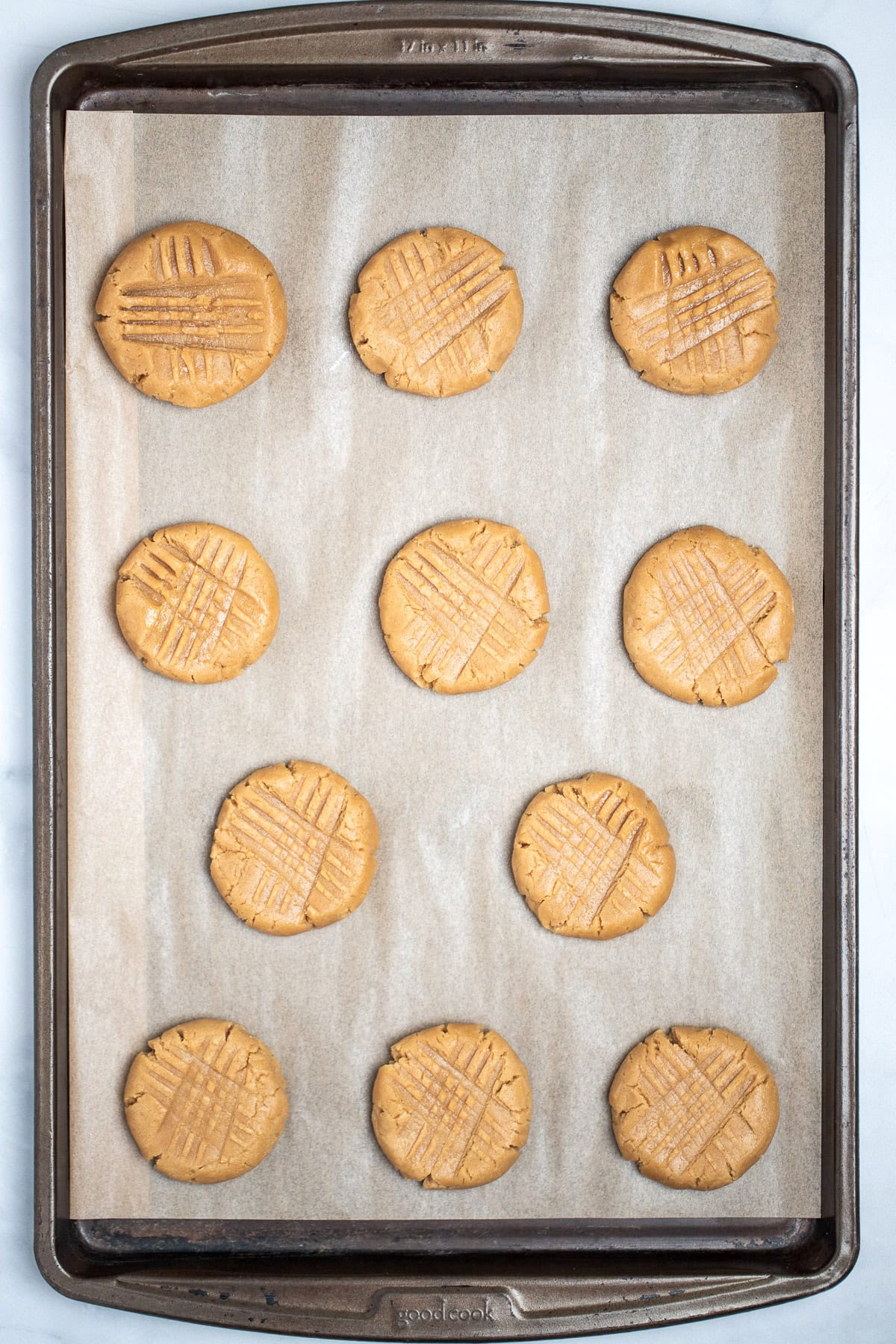 A baking tray with parchment paper and gluten free peanut butter cookies in rows of three, before baking.