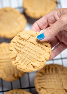 A hand holding a gluten free peanut butter cookie over a cookie rack of cooling cookies.