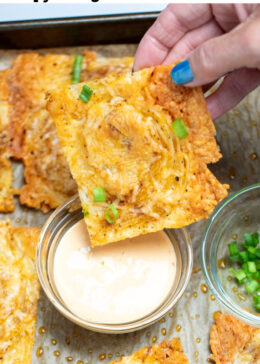 Pinterest pin with a hand dipping an onion ring chip into a small bowl of sriracha aioli, on a sheet pan of more chips topped with chopped green onion.