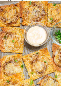 Pinterest pin with a sheet pan of parmesan onion ring chips, with a small bowl of sriracha aioli, topped with chopped green onions.