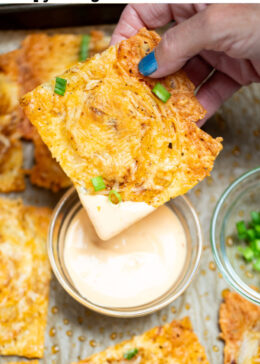 Pinterest pin with a hand dipping an onion ring chip into a small bowl of sriracha aioli, on a sheet pan with more chips.