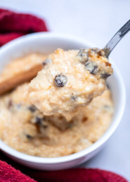 A bowl of rice pudding on a table next to a dish towel, with a spoon lifting up some pudding.